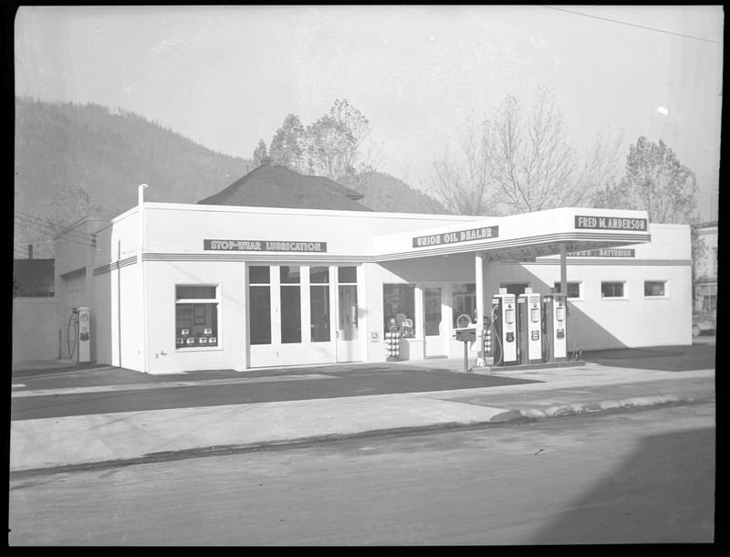 Photo of the Union Oil Dealer building. Along the exterior wall of the building there are several signs. On the left above the garage which doors are closed reads, "Stop-wear lubrication," above the gasoline pumps are two signs, "Union Oil Dealer," and "Fred M. Anderson," and on the last stretch of wall reads, "Tires; Batteries."