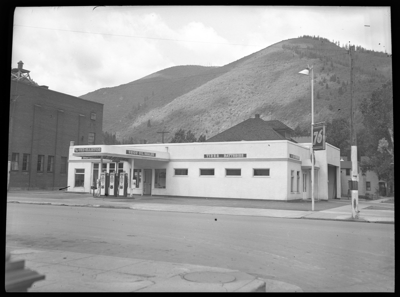 Photo of the Union Oil Dealer building. Along the exterior wall of the building there are several signs. Above the gasoline pumps are two signs, "TM.-Tex-Elliston," and "Union Oil Dealer," and on the last stretch of wall reads, "Tires; Batteries." Another garage in the building is visible on another wall.