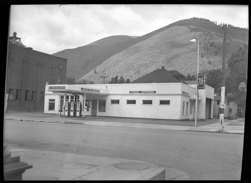 Photo of the Union Oil Dealer building. Along the exterior wall of the building there are several signs. Above the gasoline pumps are two signs, "TM.-Tex-Elliston," and "Union Oil Dealer," and on the last stretch of wall reads, "Tires; Batteries." Another garage in the building is visible on another wall.