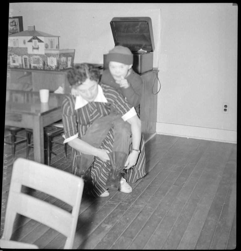 Photo of a woman helping a young boy put on his shoes inside the Opportunity School. The woman is sitting on a chair and has the child sat on her knee as she helps him.