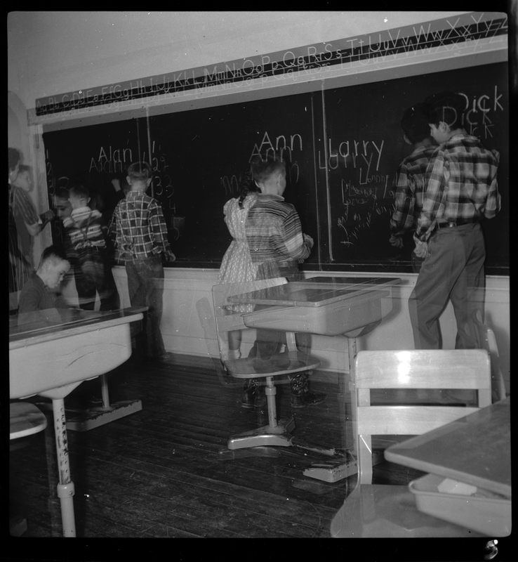Photo of a number of children writing on the blackboard at the Opportunity School. Parts of the photo have doubled, giving the illusion of seeing double.