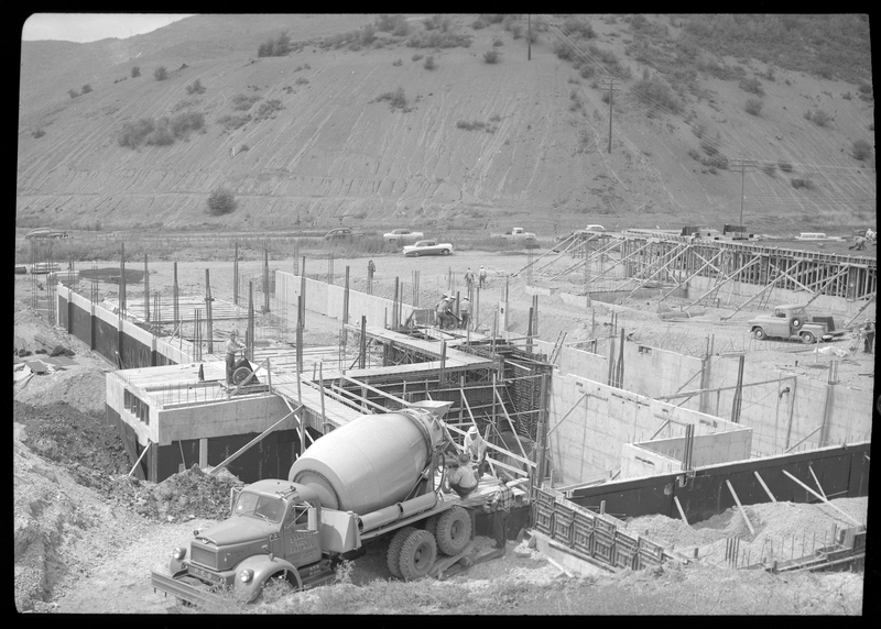 Photo of the ongoing construction of a hospital in Kellogg, Idaho that features a concrete mixing truck from Zanetti Bros. Several construction workers are visible throughout the area, which mostly just has the foundation laid down. Cars and trucks are visible in the background.