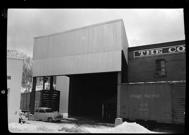 Photo of an unidentified building that has two Union Pacific train cars next to it and a car parked there as well. There is snow on the ground.