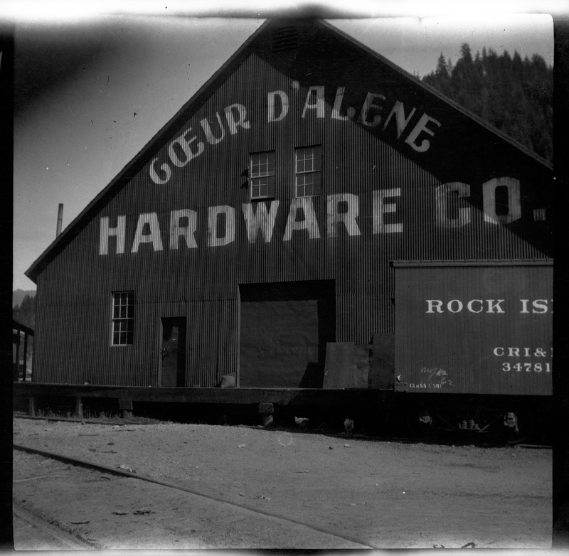 Photo of the exterior of the Coeur d'Alene Hardware Company building. The name of the business is painted on the outside, and part of a sign that reads "Rock is" is visible