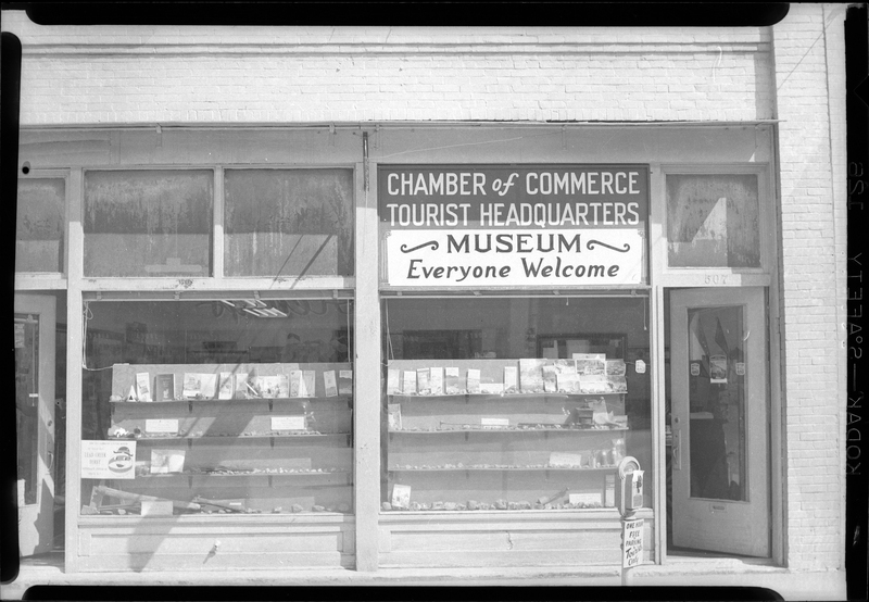 Photo of the exterior storefront of the Wallace Chamber of Commerce building. The front door is open and there is a sign that reads "Chamber of Commerce; Tourist Headquarters; Museum; Everyone Welcome."