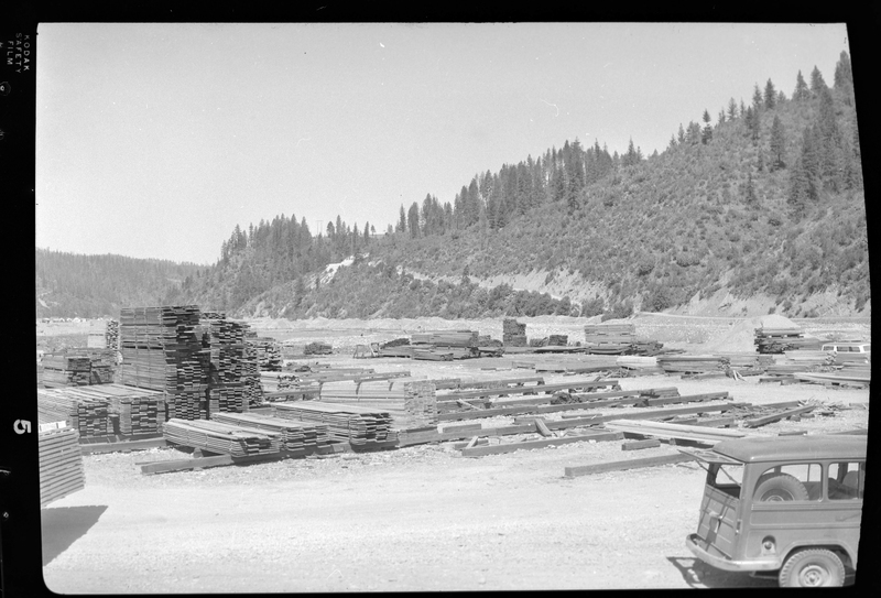 Photo of the Osburn Lumber Company lumber yard, pull of lumber piles. There is car partially in frame as well.