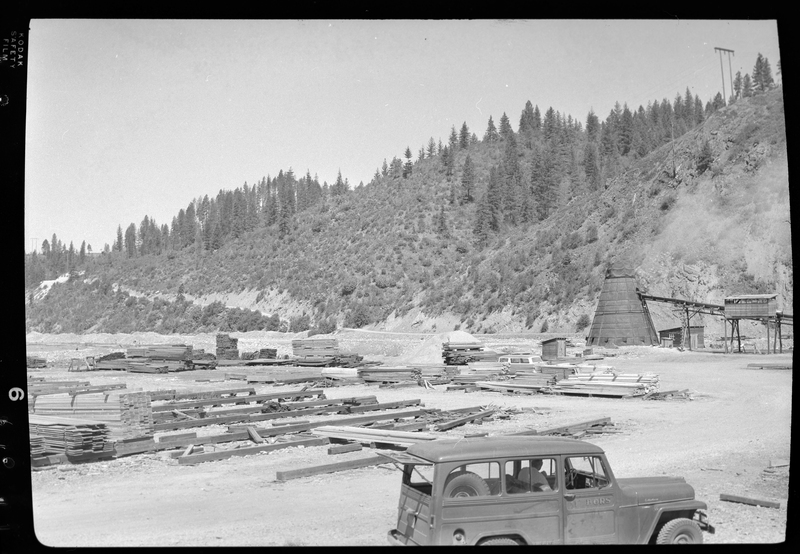 Photo of the Osburn Lumber Company lumber yard, pull of lumber piles. There is car and some machinery as well.