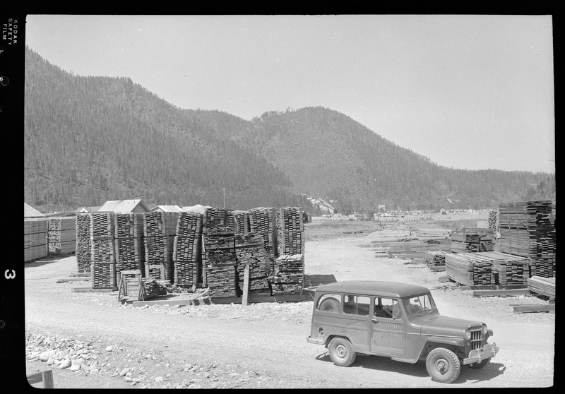 Photo of the Osburn Lumber Company lumber yard, pull of lumber piles. There is car partially visible as well.