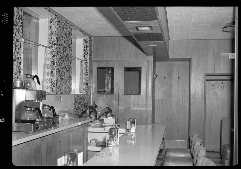 Photo of a man sitting at the counter inside of the Pacific Hotel Cafe. He is sitting by the front doors and appears to be eating.