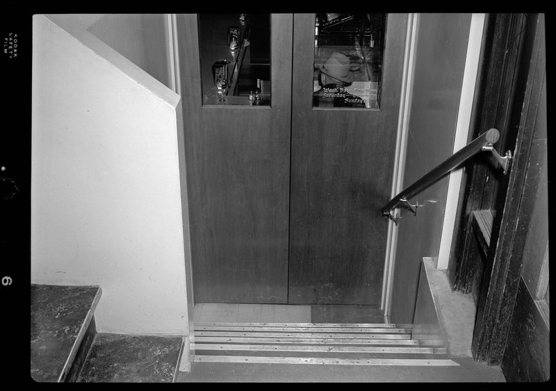 Photo of the stairs that lead down to the doors of the Hotel Pacific Cafe. On the window of the door is a decal reading "Week days 5am-11pm; Saturday 6am-9pm; Sunday."