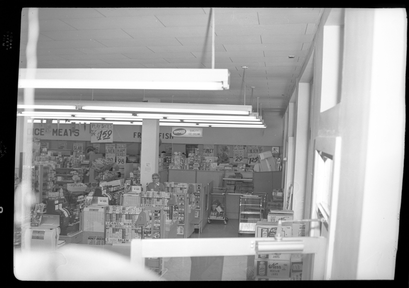 Photo of the interior of the Food Center Thrift Store. Stocked shelves line the room and a single cashier is visible at check out.