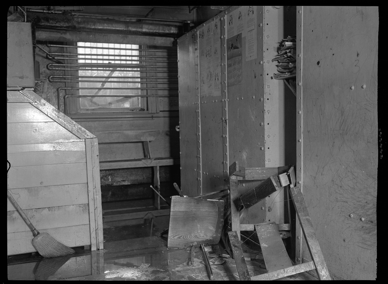 Photo of the inside of the Shoshone County Jail (in the basement of the Wallace Courthouse). There is a lot of water pooled on the floor and some of the furniture appears to be overturned.