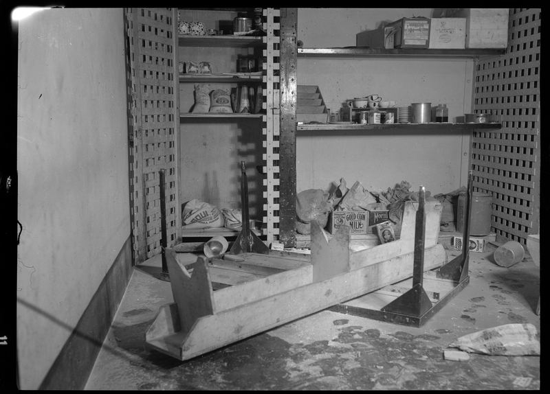 Photo of the inside of the Shoshone County Jail (in the basement of the Wallace Courthouse). Cabinets storing food products and silverware are open, and a bench and table are upside down on the floor in front of them.