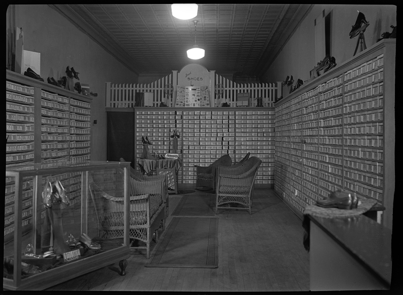 Photo of the interior of Murphy's Bootery, later renamed Pullman Bootery. There are some chairs throughout the shop and the walls are lined with shelves of shoe boxes.