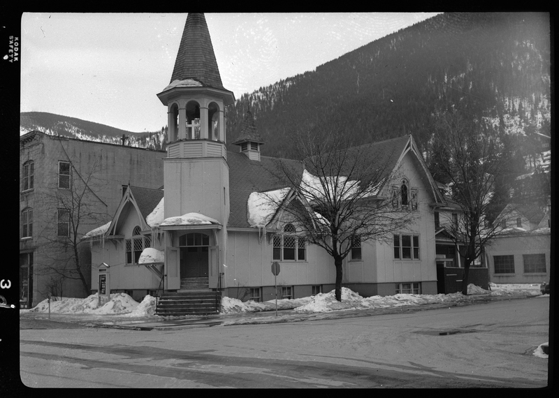 Photo of a church building on a street corner. There are a few trees along the sidewalk, and there is melting snow on the roof and ground of the church.