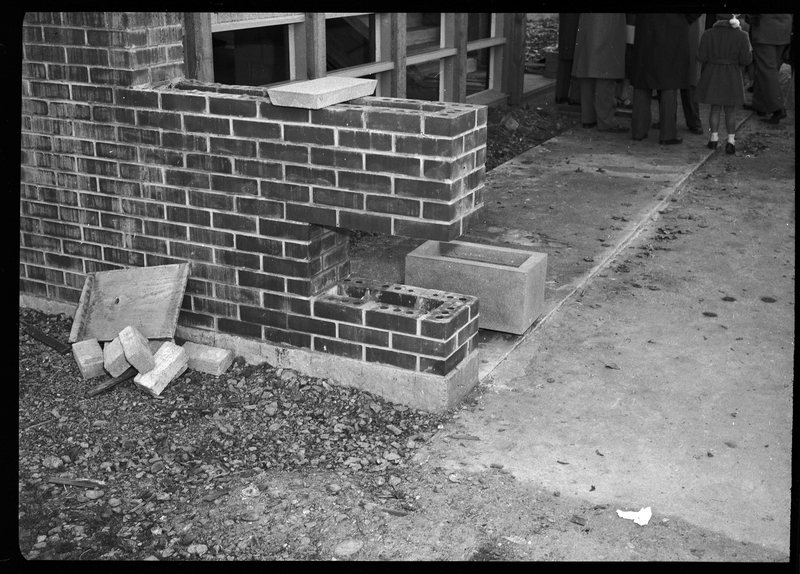 Photo of an unidentified building under construction. There is a cut out section of a brick wall and a cinder block next to it to be placed in the opening.