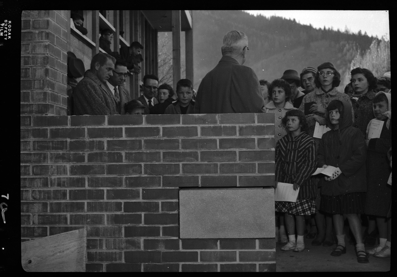 Photo of an unidentified man addressing a small crowd of people outside of a building. There is a cinder block placed in a brick wall that was just added in pg83-b01-f04-052_015.jpg.