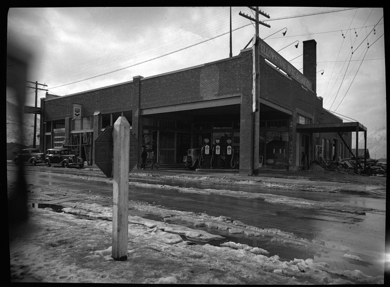 Photo of the Yellowstone Garage building. There are gas pumps underneath the building's overhand, and a few cars parked around the building. There is snow on the ground.