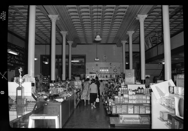 Photo of a small group of people, mostly women, shopping inside of the Coeur d'Alene Hardware Store. There are shelves with various hardware equipment throughout the store for sale.