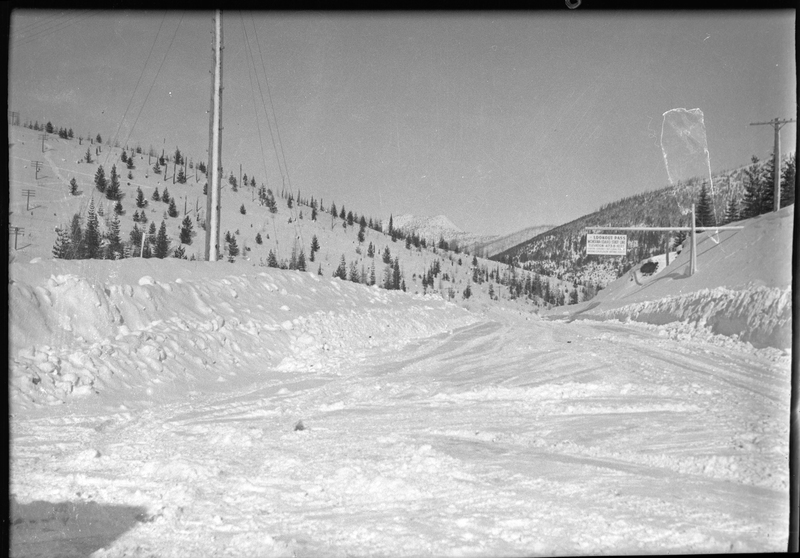 Photo of the snow covered road at Lookout pass. There is a sign that reads "Lookout Pass; Montana-Idaho State Line; Elevation 4738 Feet" that hangs over the road.