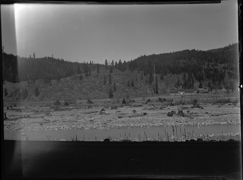 Photo of the Strope Addition to the west side of Wallace, Idaho. There is a open field with a house pictured. There is what appears to be a river between the photographer and the subject area.