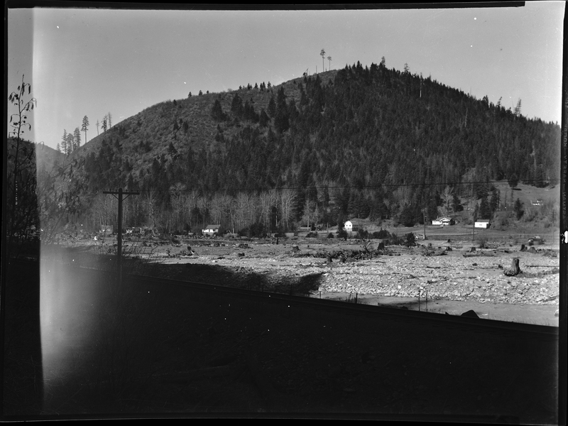 Photo of the Strope Addition to the west side of Wallace, Idaho. There is a open field with several houses pictured. There is what appears to be a river between the photographer and the subject area.