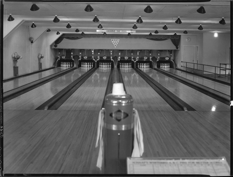 Photo of the Wallace Bowling Alley lanes looking towards where the pins are. There is a sign on the wall over the lanes that reads, "Please observe the foul line."