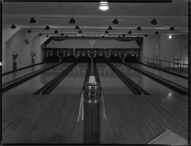 Photo of the Wallace Bowling Alley lanes looking towards where the pins would be. There is a sign on the wall over the lanes that reads, "Please observe the foul line." 