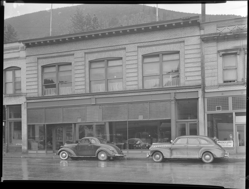 Photo of an unknown building (possibly the Labor Building on Bank Street) including the Wallace Miner and Employment Office F. M. & S. Company. There are two cars parked on the side of the road in front of the building.