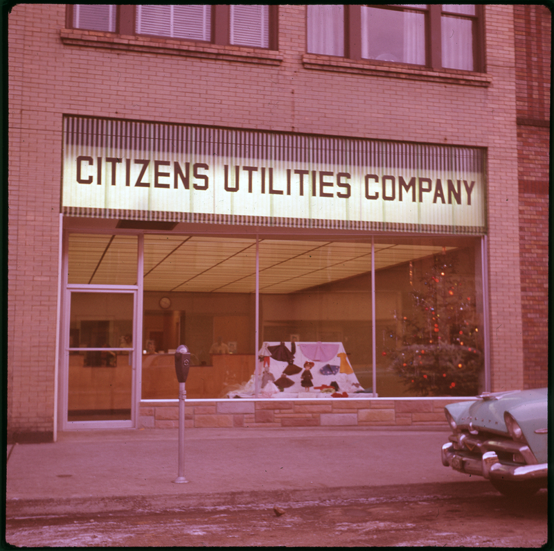 Photo of the exterior of the Citizens Utilities Company building. The lights are on inside of the building.