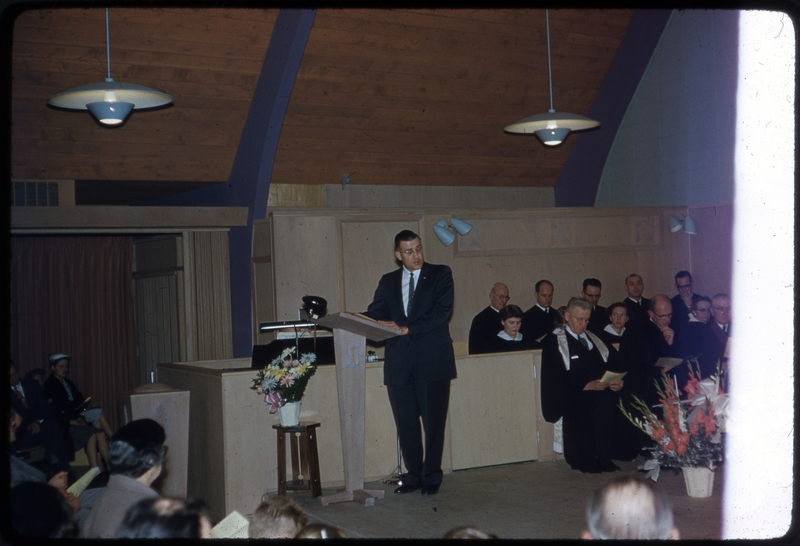 Color photo of a man addressing the crowd at the Congregational Church dedication gathering. The right side of the negative is badly damaged.