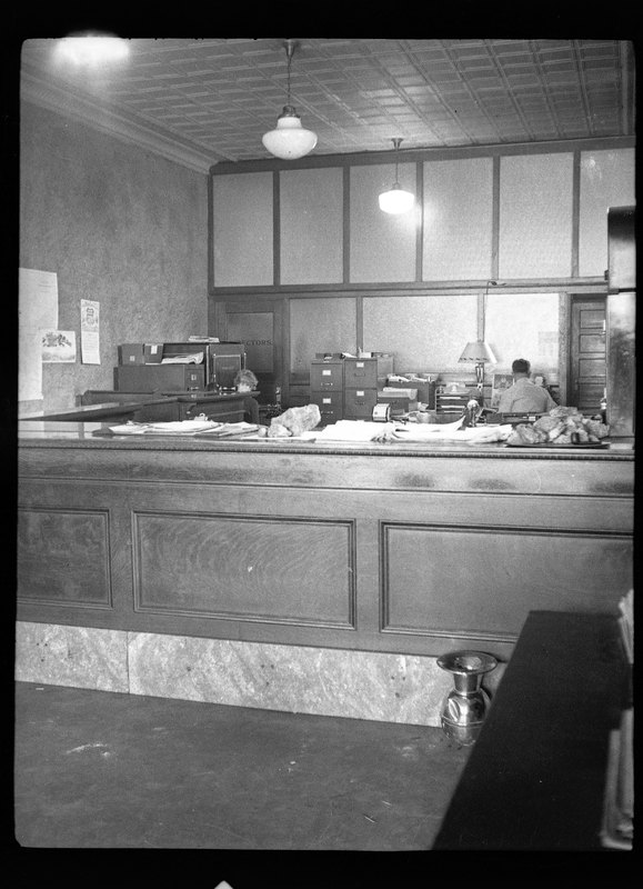 Photo of the interior of an unidentified office. There are two people behind the front counter.