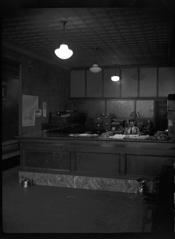 Photo of the interior of an unidentified office. There is a man sitting behind the front counter.