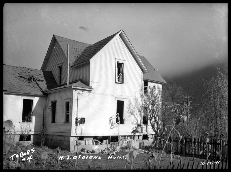 Exterior damage to N. J. Osborne's home after the Sunshine Mine powderhouse explosion. There is visible damage to the windows, foundation, and roof.