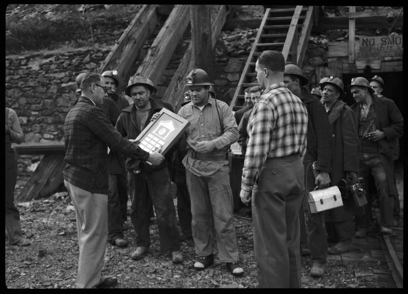 Group of miners from Hecla Mining Company receiving safety award. Two men present the award to the miners.