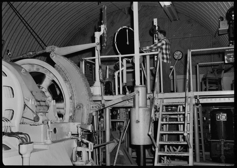 The interior of the Lucky Friday mine hoist room. Signs describe the signal and bell system. There is a man operating the machinery.