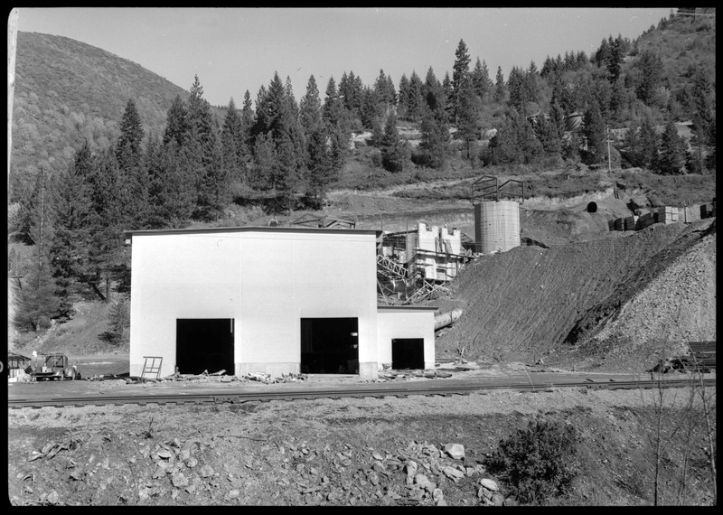 The exterior of Lucky Friday mill facilities and buildings which are under construction, including what appears to be a silo for holding mineral materials. Workers are on the roof of a building.