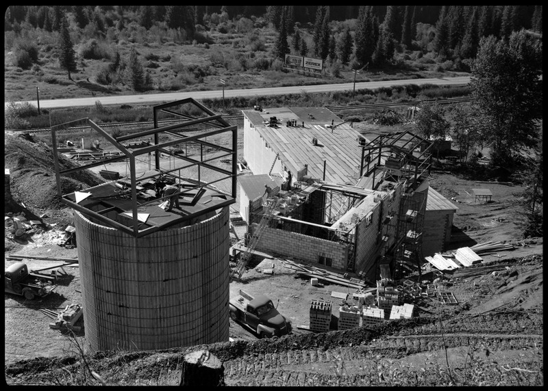 The exterior of Lucky Friday mill facilities and buildings which are under construction, including what appears to be silos for holding mineral materials. Workers are on several of the structures and facilities. 