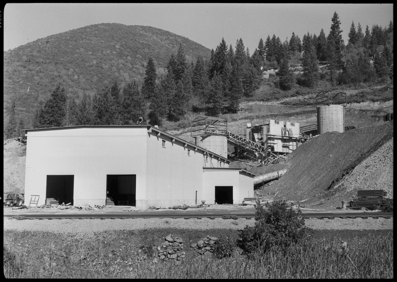 The exterior of Lucky Friday mill facilities and buildings, including what appears to be silos for holding mineral materials. Workers are doing construction or maintenance on several of the structures and facilities. 