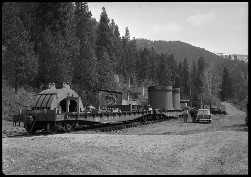 A disassembled mine hoist on a train at the Lucky Friday Mine near Mullan, ID. A handful of people stand between the train and a car.