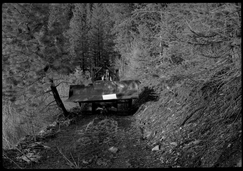 A couple men moving a piece of machinery through a heavily wooded area.