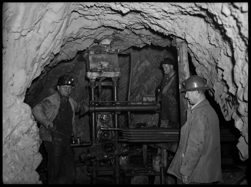 Three miners working inside of Silverton Mine. They are working with a piece of machinery.