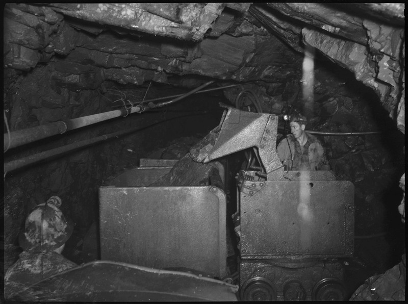 Several miners working in a tunnel of an unidentified mine inside of mine carts.