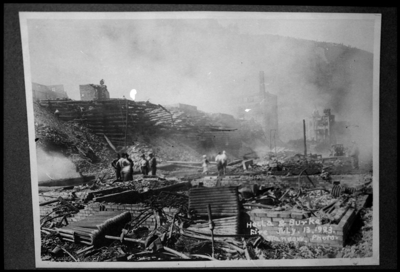 Image of a photograph of the Hecla and Burke fire. There are several people looking among the wreckage.