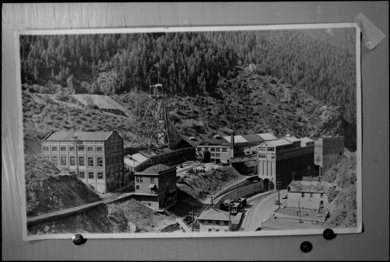 Image of a photograph that overlooks Hecla Mine in Burke, Idaho. Some of the buildings are visible, as are railroad tracks.