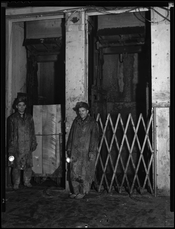 Two men working inside of an unidentified mine. They appear to be standing next to elevators.