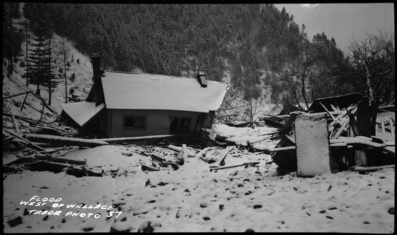 The damage caused by the Wallace, Idaho flood. Its a photo of a building, probably a house, west of Wallace that was knocked down by the flood. The area is also covered in snow.