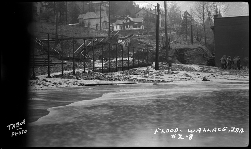 The flood in Wallace, Idaho. There are people standing in the background and part of the photo is damaged. There is some snow on the ground.
