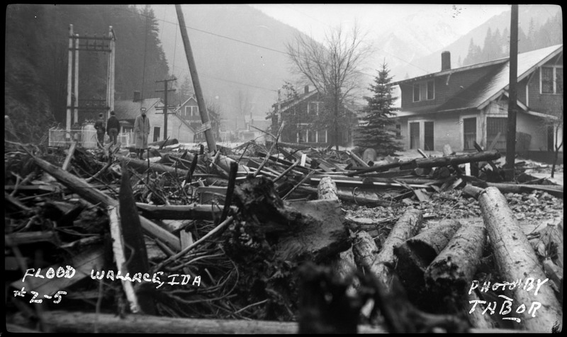 The damage done by a flood in Wallace, Idaho. There are people standing in the background, with the focus on the building damage.