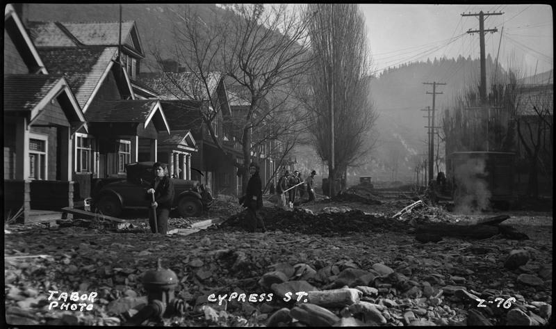 Cypress Street in Wallace, Idaho after the flood. People are standing amongst the damage to try and clear it up.
